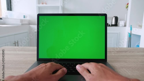 Point of view, man sitting at kitchen table and using laptop computer with green screen chroma key, freelancer working from home