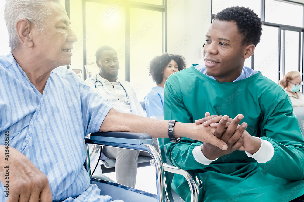 Fototapeta premium African male doctor holding patient man who sitting in wheelchair to encourage in hospital
