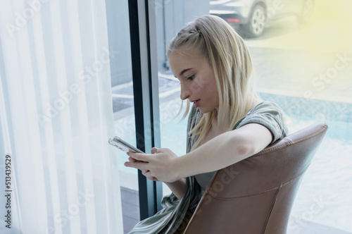 Young Caucasian teenage girl using smartphone texting,chatting  with friends,  girl looking at cellphone shopping online photo