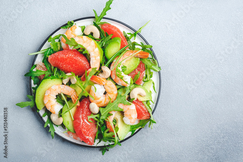 Fresh summer salad with shrimps, avocado, pink grapefruit, arugula and cashews. Gray stone kitchen table background, top view, copy space