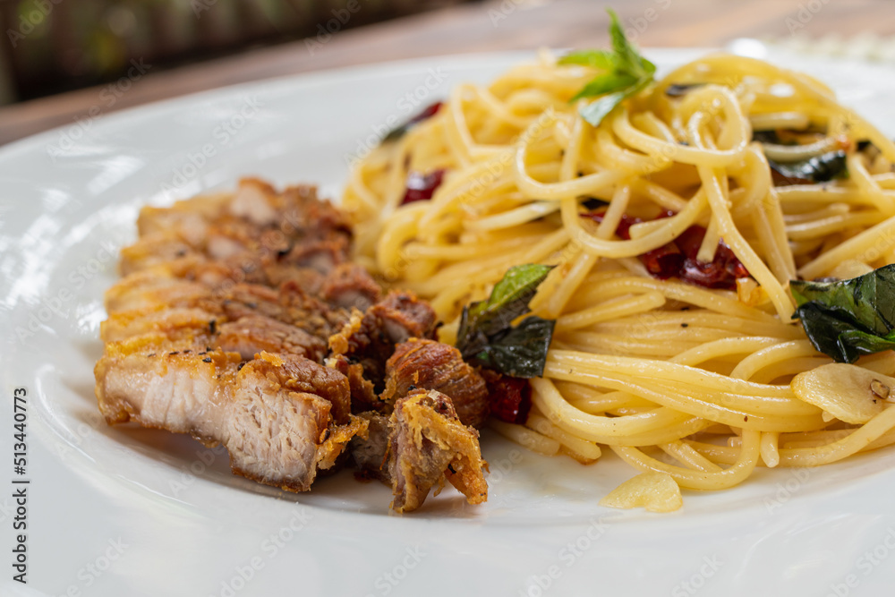 Thai-style stir-fried spaghetti with dried chilli sauce and hot, tender and delicious pork cutlets are served in a white plate on a wooden table, resulting in a spicy spaghetti and fragrant pork cutle Thai-style stir-fried spaghetti with dried chilli sauce and hot, tender and delicious pork cutlets are served in a white plate on a wooden table, resulting in a spicy spaghetti and fragrant pork cutle