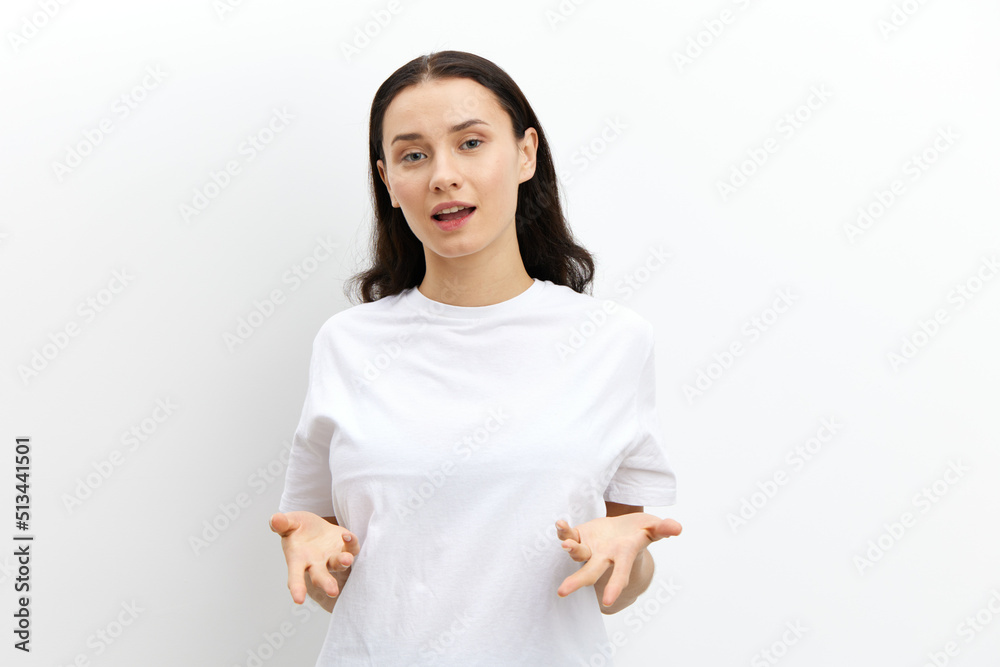 a beautiful, sweet, attractive woman with long dark hair stands on a white background in a white T-shirt and actively gestures with her hands looking at the camera a beautiful, sweet, attractive woman with long dark hair stands on a white background in a white T-shirt and actively gestures with her hands looking at the camera