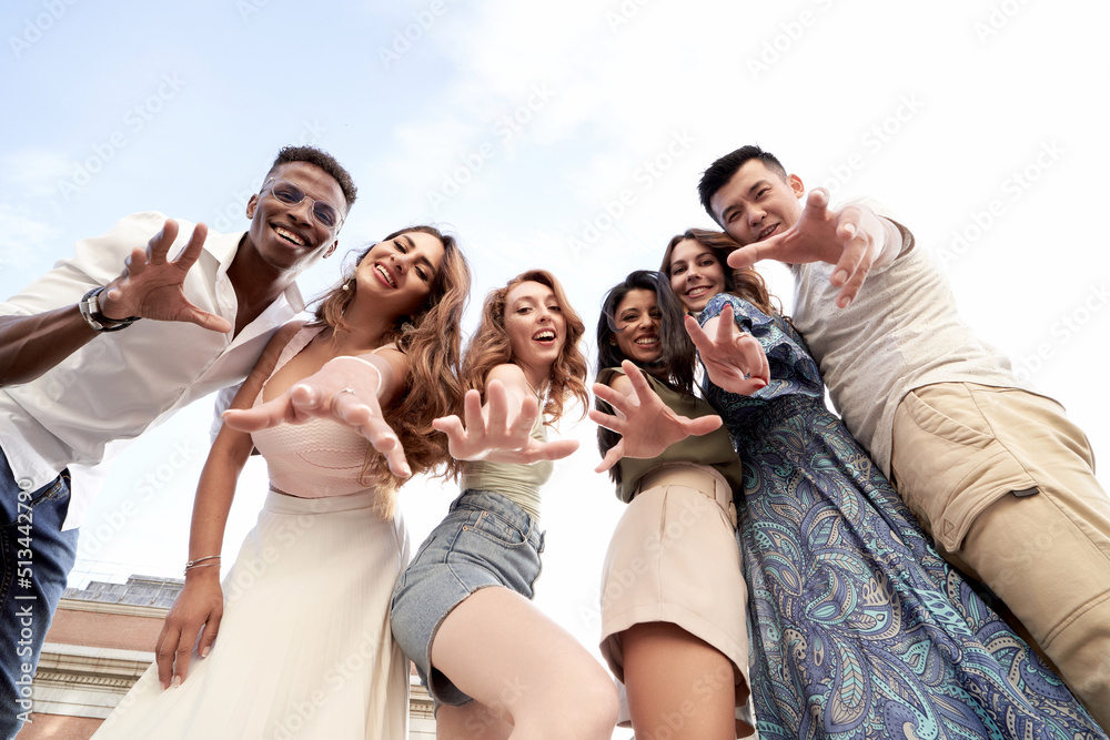 Low angle view of a group of multi-ethnic friends looking at camera and smiling while posing together outdoors. Friendship concept.