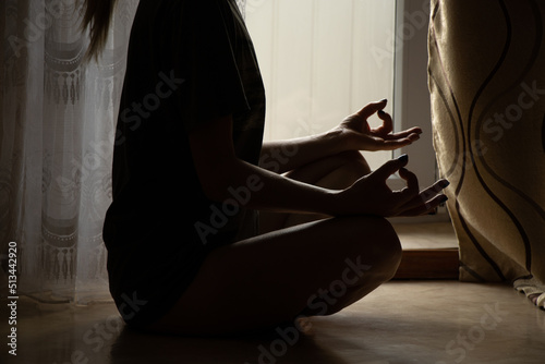 The girl meditates in the apartment sitting on the floor near the window, yoga and meditation
