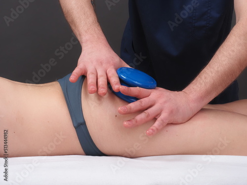 The master masseur performs an anti-cellulite massage on the girl's hips with rubber jars for smooth skin and slimness