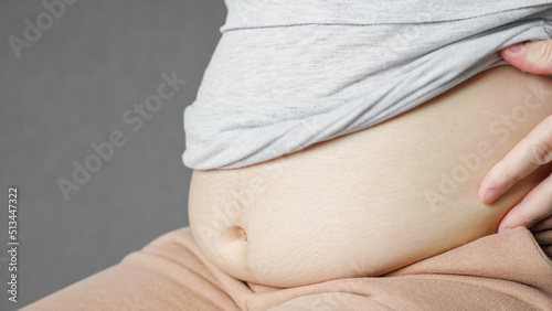 Woman rolls out corrective pants and releases fat belly. Flabby female belly after pregnancy. Woman measures fat on stomach touching sagging skin closeup