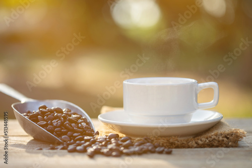 Cup of coffee and coffee beans on outdoor wooden table in morning sunlight and bokeh background