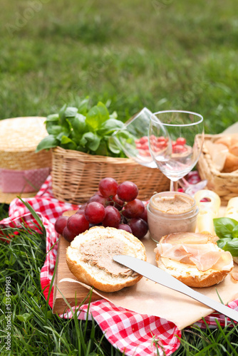 Picnic blanket with wineglasses and food on green grass