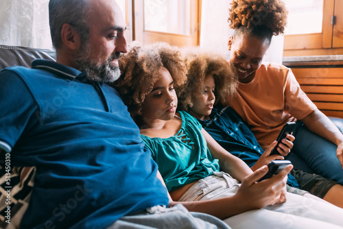 Parents looking at children using smart phones sitting on sofa photo