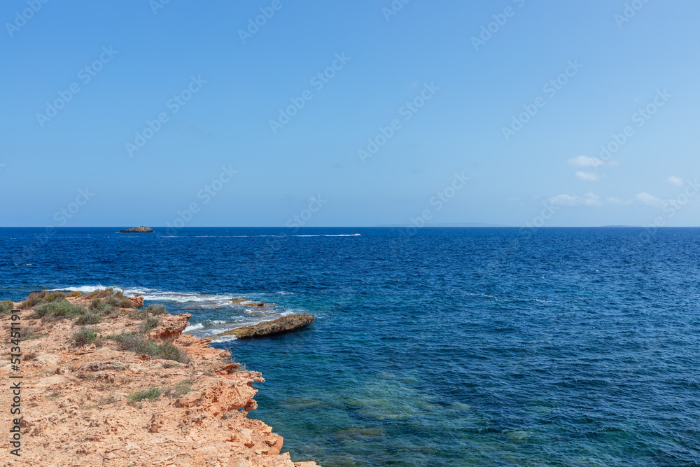 Tiny motorboat crosses waters of bay near Ibiza island, sea has a beautiful deep blue color, Balearic Islands, Spain