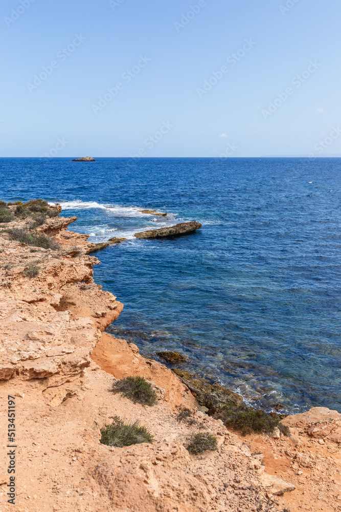 Orange color of coastal cliff, blue color of sea water and pale blue color of  clear sky. Ibiza, Balearic Islands, Spain (vertical shot)