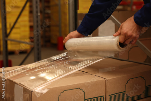 Billede på lærred Worker wrapping boxes in stretch film at warehouse, closeup