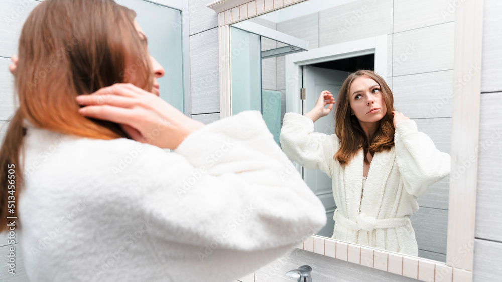 Morning of a young woman. A model in a white coat in front of a mirror. Bright bathroom with a new renovation Morning of a young woman. A model in a white coat in front of a mirror. Bright bathroom with a new renovation