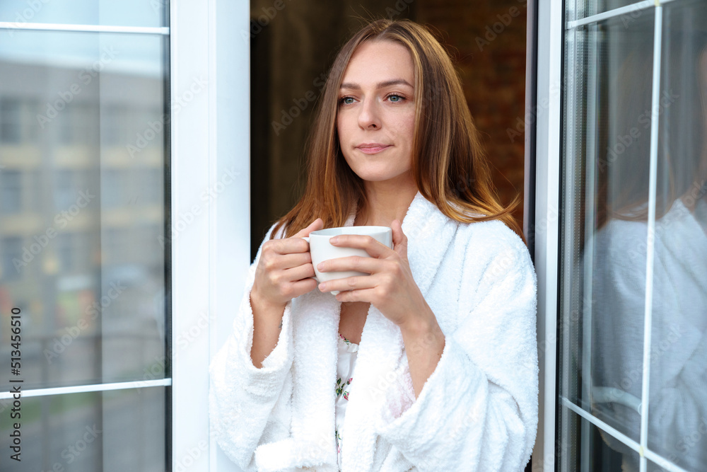 A young woman is drinking coffee on the hotel balcony. A model in a white bathrobe enjoys the morning A young woman is drinking coffee on the hotel balcony. A model in a white bathrobe enjoys the morning