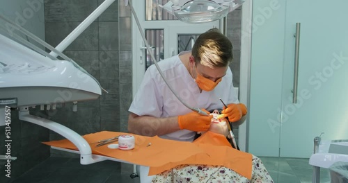 specialist dentist male in gloves and mask makes professional hygiene procedure for teeth of patient who with dilator in mouth lies in stomatology chair in clinic