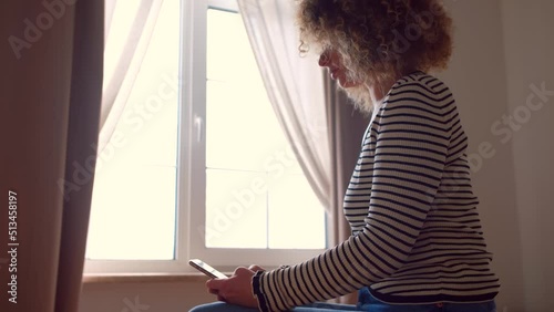 Young Ukrainian woman browsing mobile phone in dark room. Curly white female using modern smartphone  photo