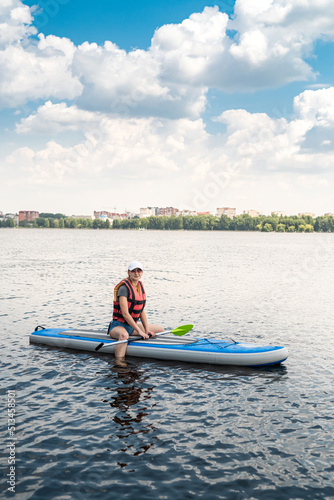  young woman wear life vest paddle boarding on a lovely lake at summer hot day