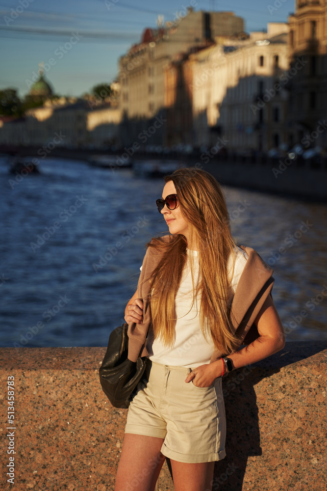 beautiful young woman stands on a bridge in sunglasses in a european city in the summer in the sun beautiful young woman stands on a bridge in sunglasses in a european city in the summer in the sun