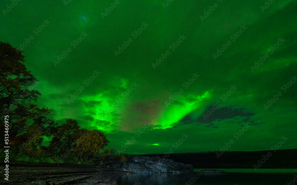 Northern lights over the plain lake and stone beach