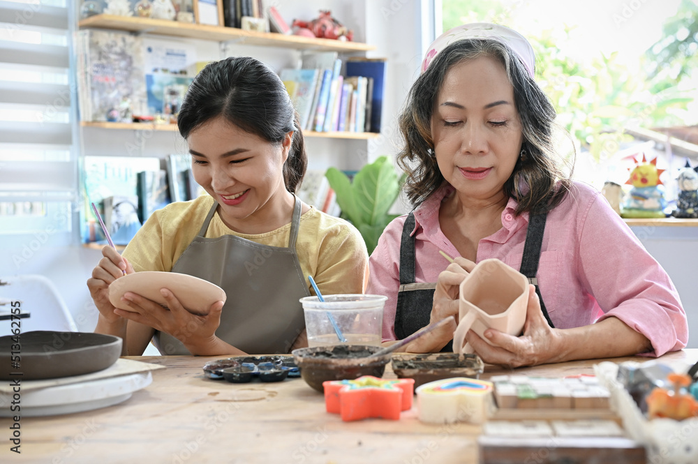 Relaxed asian aged woman and young woman concentrated painting their handmade ceramic cup