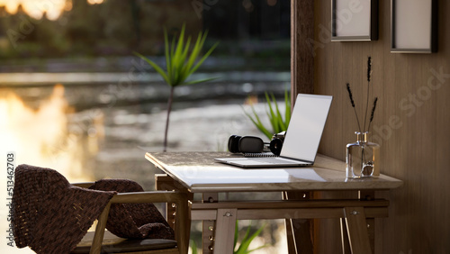 Comfortable wooden home workplace interior with portable laptop on table, window with lake view.