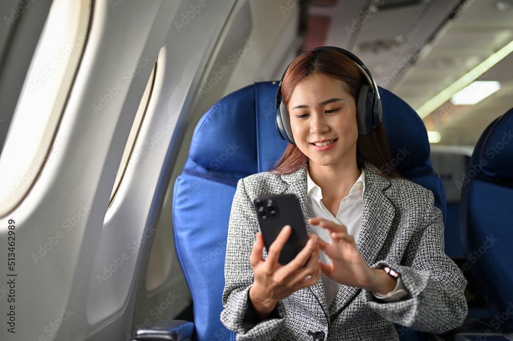 Asian businesswoman using smartphone, listening to music on headphones ...