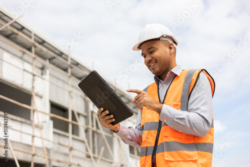 Confident asian engineer man Using tablet for checking and maintenance to inspection at modern home building construction. Architect working with white safety helmet in construction site