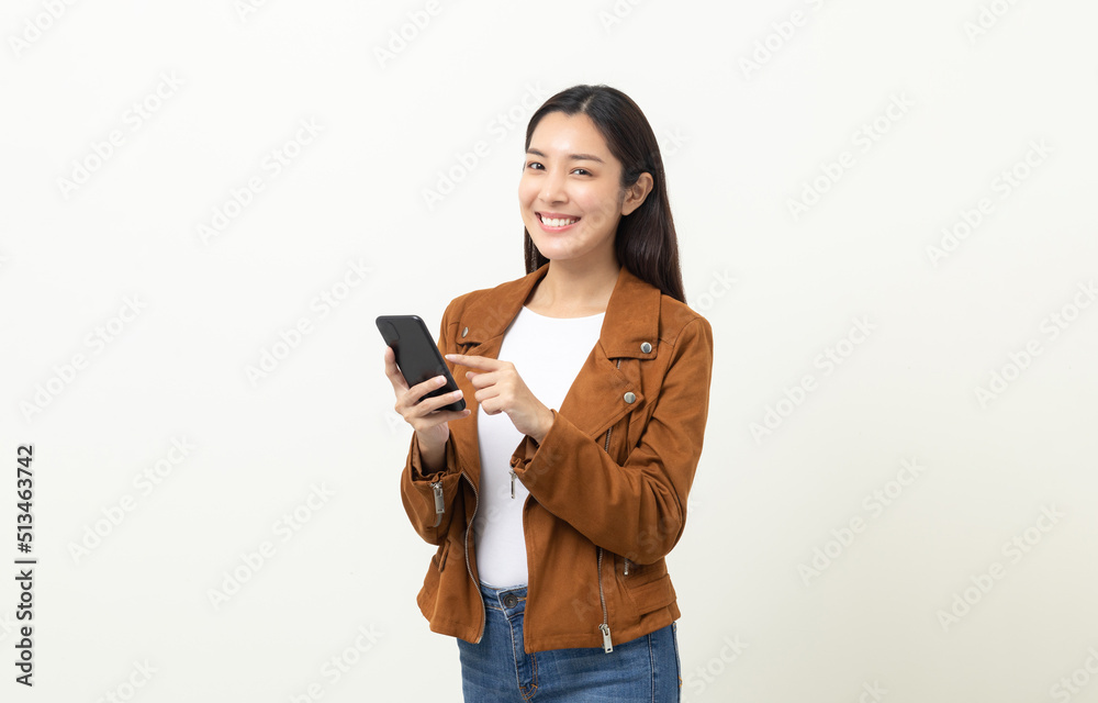 Pretty young asian woman using smartphone standing on isolated white background. She texting on cell phone. Dressing with jacket and jean. Pretty young asian woman using smartphone standing on isolated white background. She texting on cell phone. Dressing with jacket and jean.