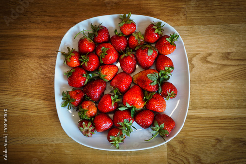 Strawberries on plate, wooden table - top view