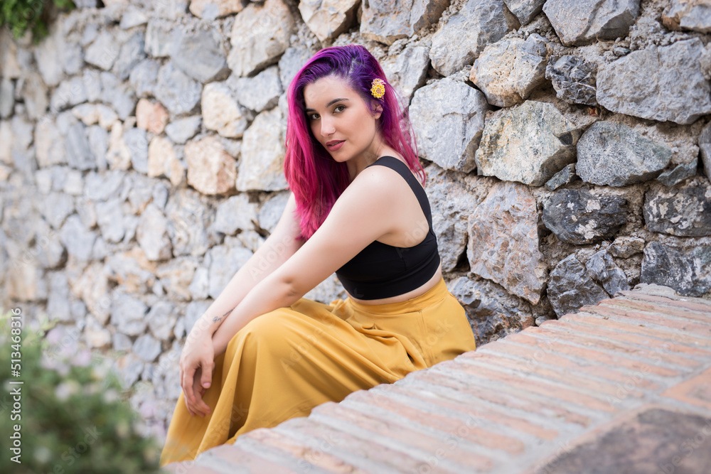 Young woman sitting near stone wall
