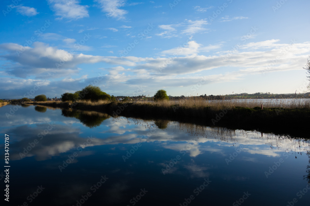 sunrise at the Exeter Ship Canal with a few clouds reflected in the still water and a clear blue sky