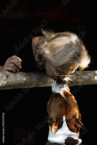 Portrait of elderly woman kissing American Staffordshire Terrier terrier dog close-up on natural background. Sunset light on face of senior. High quality photo