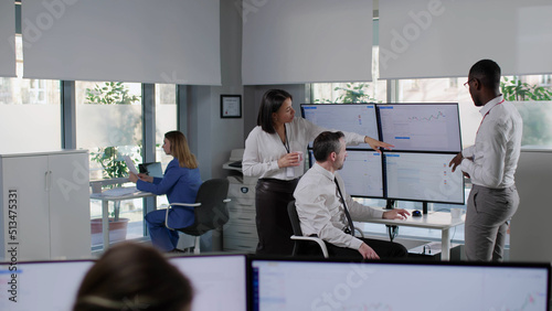 Investors discuss financial data on multiple computer screens in modern office