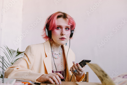 creative young woman using smartphone , listen to music at table with scetchbook and painting markers photo