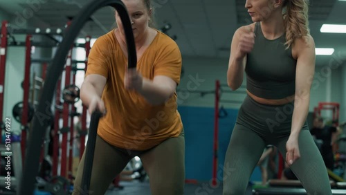 Woman with overweight exercising with battle ropes and female trainer at the gym. Shot with RED helium camera in 4K.  