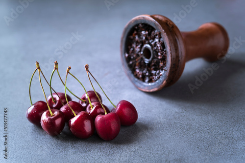 Ripe cherry and ceramic bowl full of tobacco for hookah on the gery background. Copy space