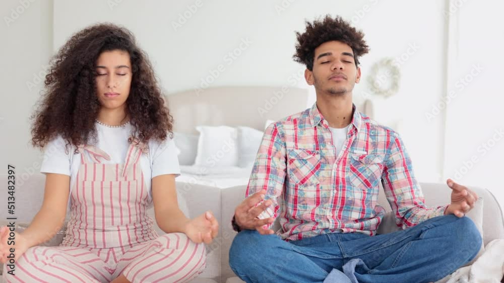 Young beautiful couple is meditating and sitting on sofa in home interior spbi. 4k Close view of young woman, man meditate with closed eyes and make mudra with hands, control breathing and sit on Young beautiful couple is meditating and sitting on sofa in home interior spbi. 4k Close view of young woman, man meditate with closed eyes and make mudra with hands, control breathing and sit on