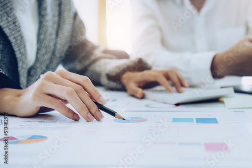 two young Asian businesswoman using their tablet computers with documents and calculator to plan marketing strategies and investments to profit from their clients