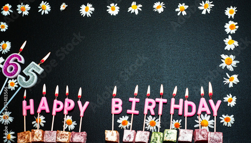 Happy birthday background with number   65. Copy space. Pink happy birthday candles on a black background. Happy birthday flower frame