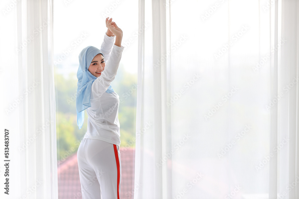 Beautiful asian woman wearing white muslim sleepwear, stretching her arms after getting up in the morning at sunrise. Cute young girl with blue hijab standing and relaxing with happy and smiling face. Beautiful asian woman wearing white muslim sleepwear, stretching her arms after getting up in the morning at sunrise. Cute young girl with blue hijab standing and relaxing with happy and smiling face.