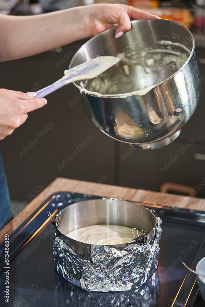 female hands shift the batter from an iron bowl with a spatula into a round iron baking dish
