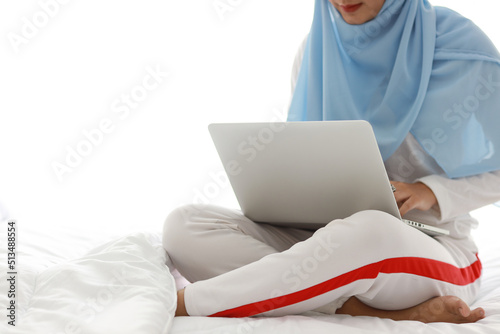 Young asian woman hands use laptop sitting on bed in bedroom. Beautiful girl in muslim sleepwear with blue hijab check order or study from notebook before go to bed. Lifestyle and technology concept