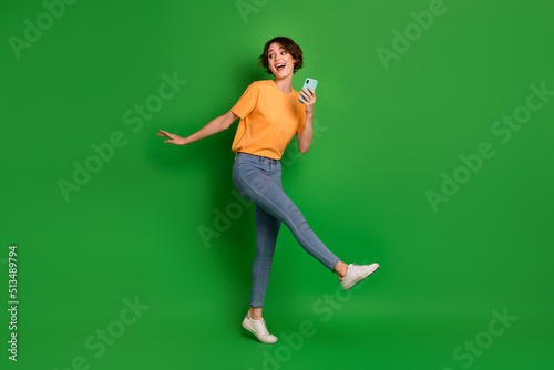 Full length photo of positive charming girl arm hold telephone look empty space isolated on green color background