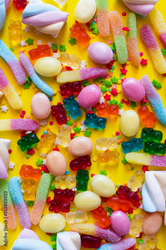Top view of colorful marshmallows and gummy bears on yellow surface.