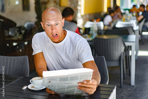 MIddle-aged man reading newspaper behind table in street cafe
