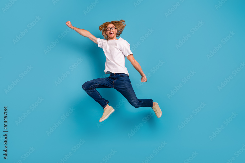 Obraz premium Full length portrait of overjoyed sporty man raise hand flight jump isolated on blue color background