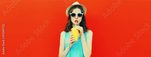 Portrait of young woman drinking fresh juice wearing summer straw hat on red background