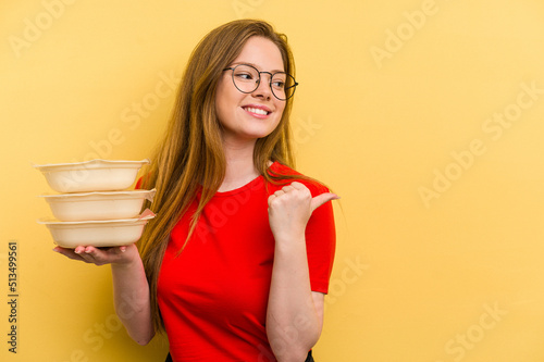 Young caucasian woman holding tupper isolated on yellow background points with thumb finger away, laughing and carefree.