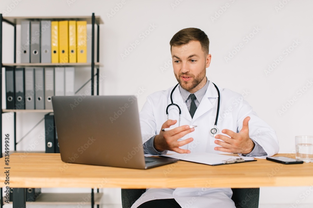 Happy male doctor watching an online medical webinar or training seminar while sitting with a laptop in the workplace. Happy male doctor watching an online medical webinar or training seminar while sitting with a laptop in the workplace.