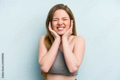 Young caucasian woman isolated on blue background covering ears with hands.